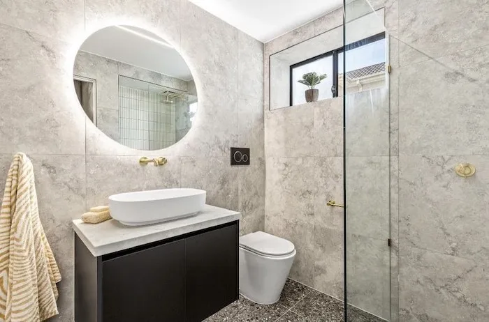 Round backlit mirror bathroom with marble tile and black vanity