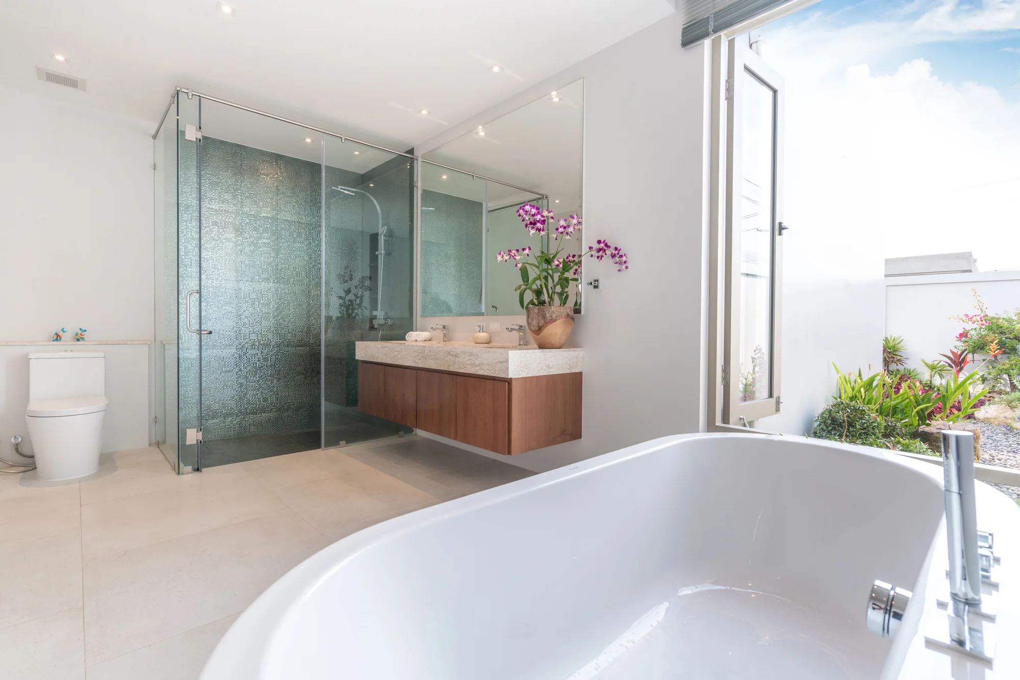 Glass-enclosed luxury ensuite with freestanding tub and garden view